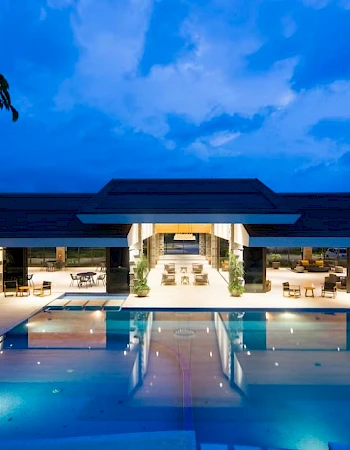 A luxurious facility with an illuminated swimming pool and modern architecture under a twilight sky.