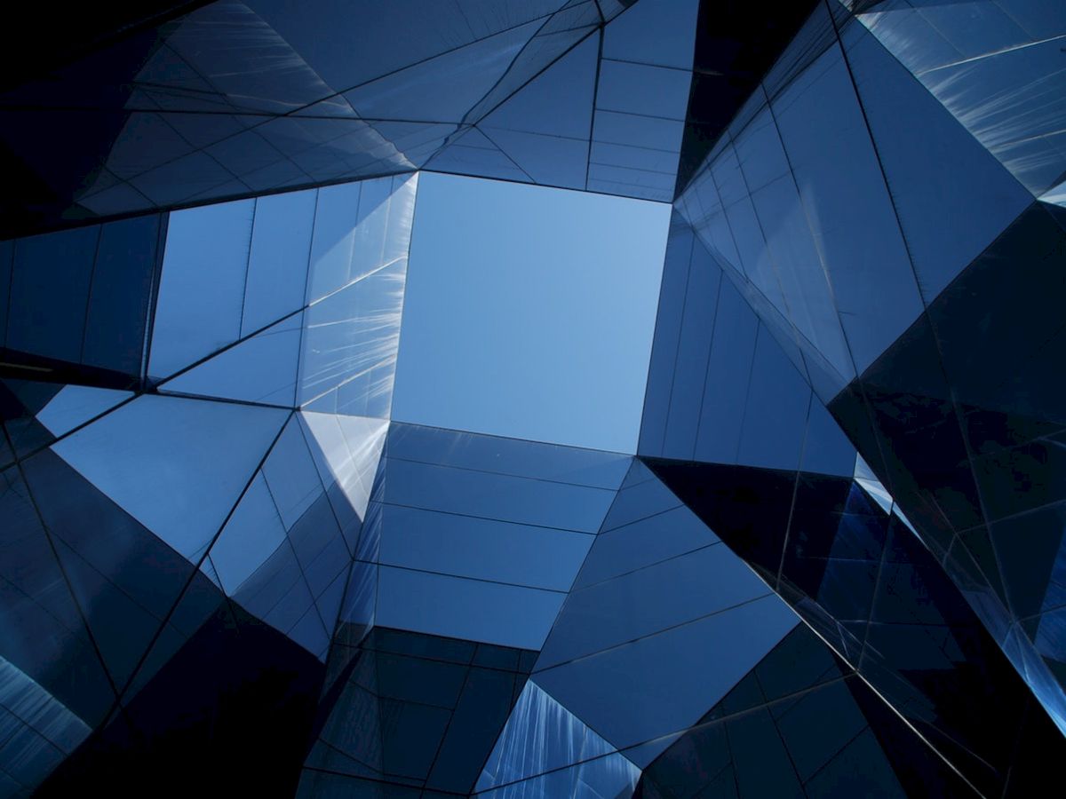 The image shows a geometric arrangement of reflective glass panels forming a skylight, with a view of the blue sky through the center.