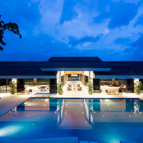 A modern building with an illuminated outdoor pool and lounge area during twilight, showcasing an inviting and luxurious atmosphere.