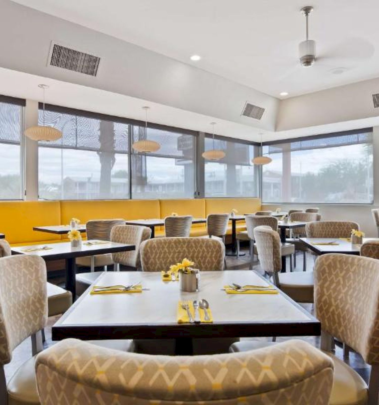 This image shows an empty restaurant dining area with modern decor, yellow booth seating, tables set with yellow napkins, and large windows.