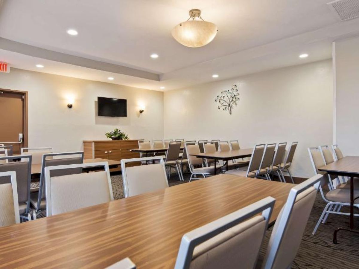 A conference room with several tables and chairs, a wall-mounted TV, a wooden cabinet with a plant, and recessed lighting.