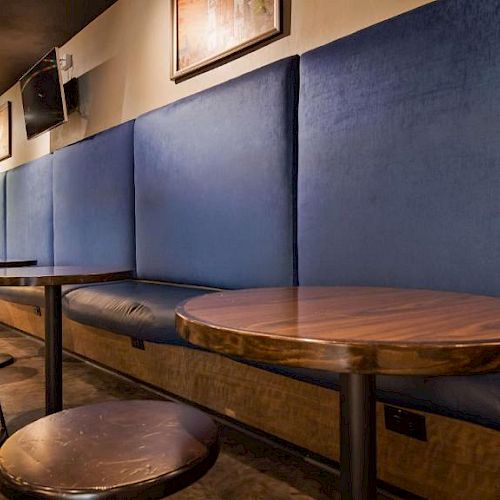 A modern café interior with round wooden tables, metal stools, and blue cushioned seating along the wall, decorated with framed art.