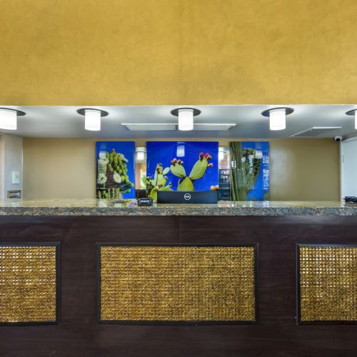 A hotel reception desk with a wooden front panel, modern overhead lights, and colorful artwork behind the counter featuring cartoon characters.