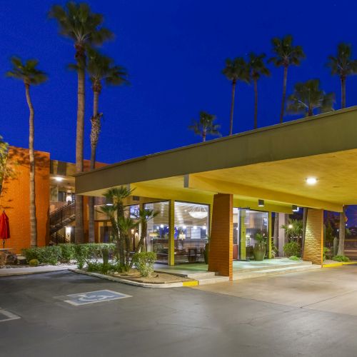 The image shows the entrance of a facility with a yellow overhang, palm trees, and a well-lit building at night.