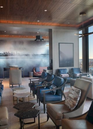 This image shows a modern lounge area with numerous comfortable chairs, large windows offering a scenic waterfront view, and a mural on the back wall.