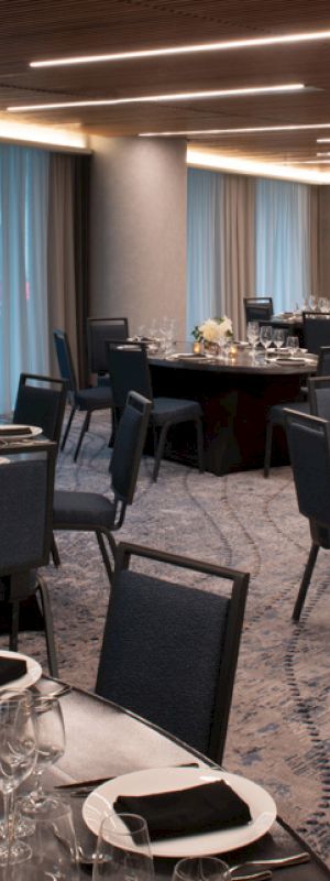 The image shows an elegant banquet hall set up for an event with round tables covered in black tablecloths, neatly arranged chairs, and dim lighting.