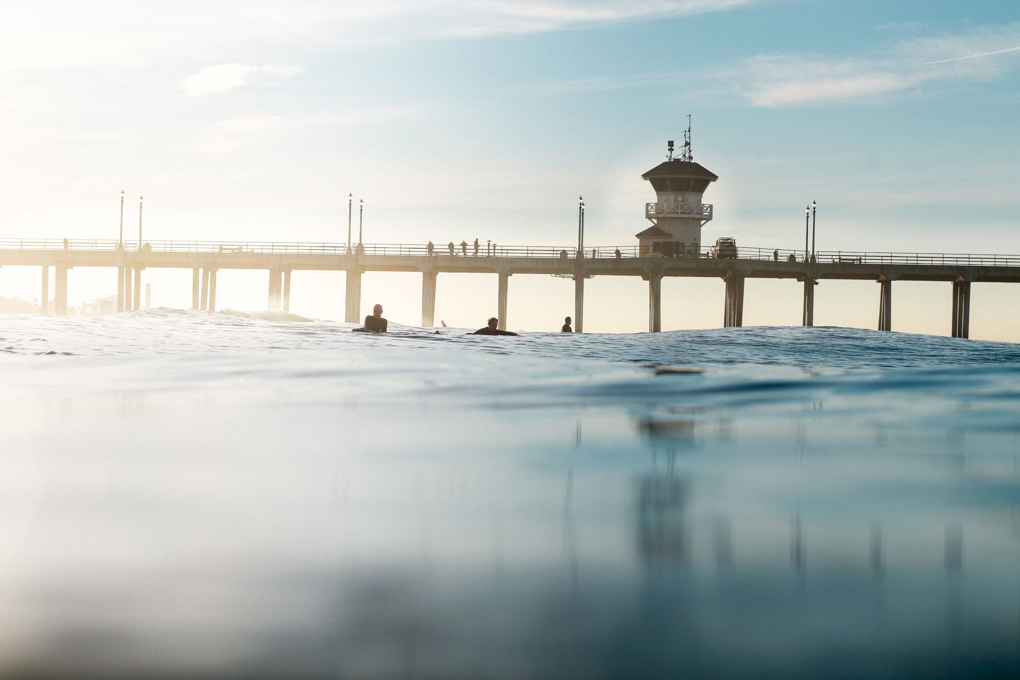 A tranquil photo shows a pier with a tower extending over calm water, with a few people seen on the pier and in the water.